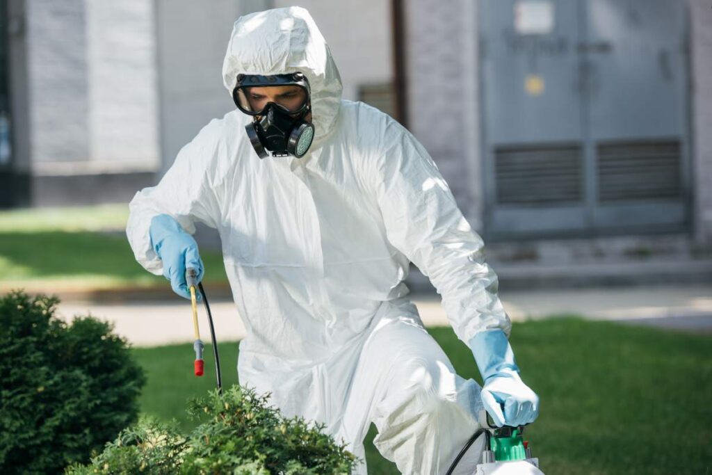 male pest control worker in uniform spraying chemicals on bush